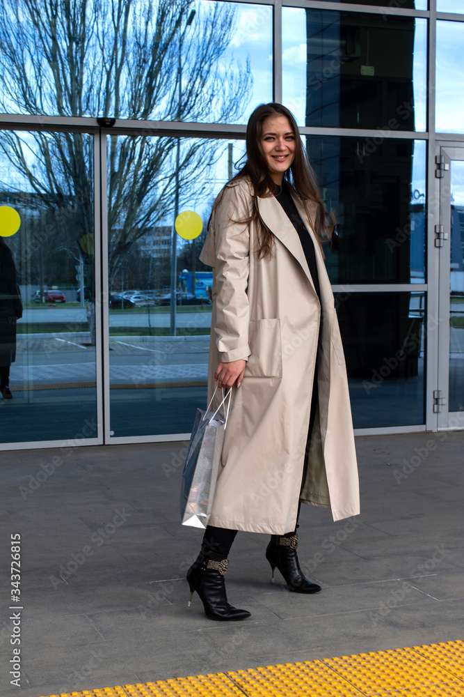young brown-haired beautiful girl with green eyes and a light trench out of the store, shopping center, shopping