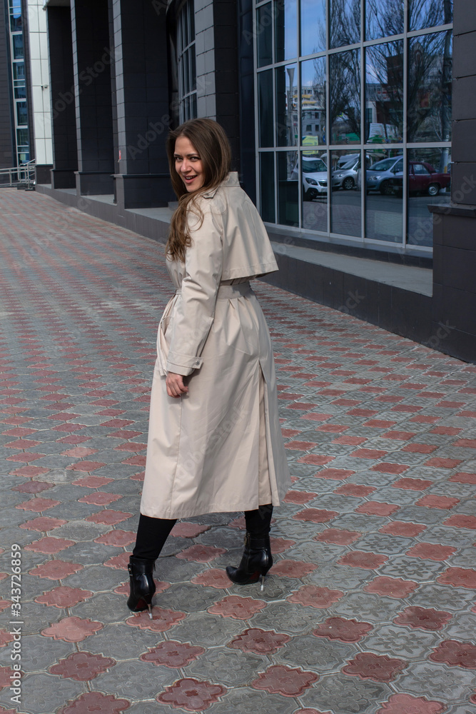 young brown-haired beautiful girl with green eyes and a light trench rear view with the coming out of the store with shopping