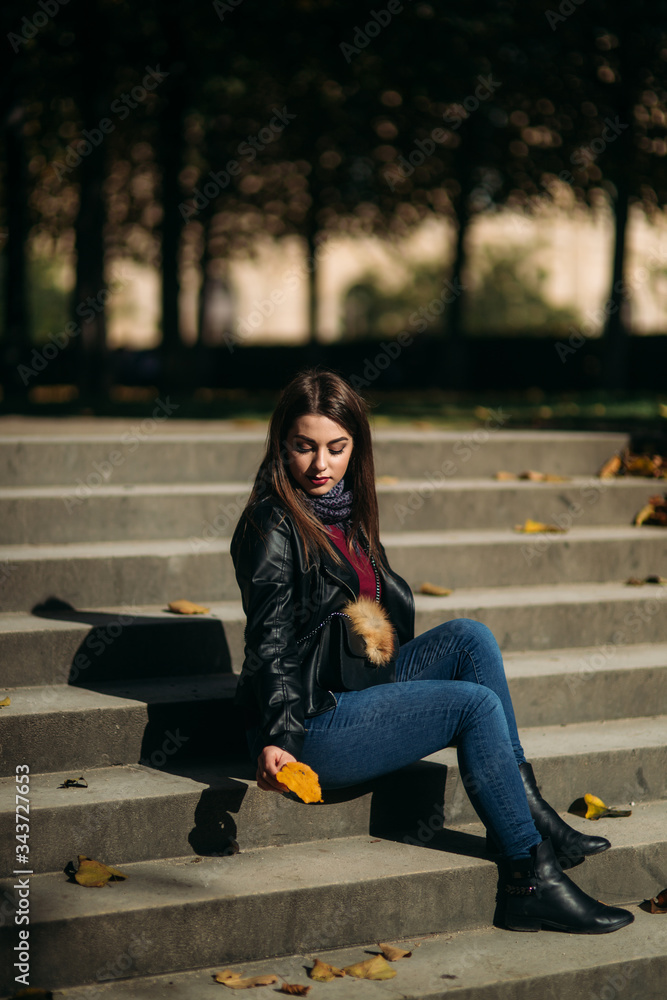 Stylish beautiful lady in a black leather jacket with a black bag and sweatshirt. Female sits on stairs Stylish beautiful lady in a black leather jacket with a black bag and sweatshirt. Female sits on stairs