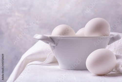 on the white linen tablecloth  in the foreground  a ceramic bowl with fresh white eggs ready for the preparation of homemade culinary recipes