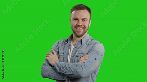Young man crossed arms on green screen and smiling. Portrait of handsome guy posing with folded arms at chroma key. 4K, UHD