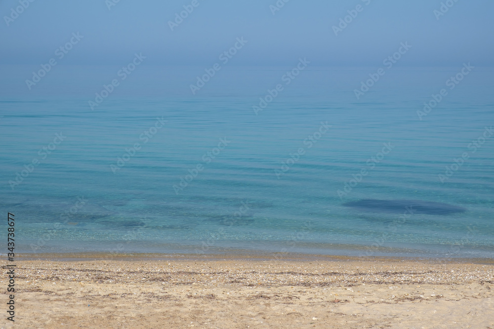 The calm surface of the sea and a deserted sandy beach. Small waves and blue sky. Halkidiki, Greece.