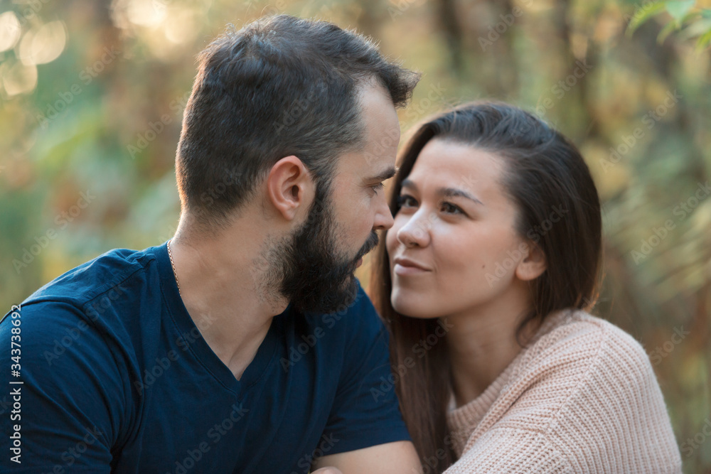 Portrait of young beautiful couple in the Park. They look at each other. In the background of leaves of trees. Portrait of young beautiful couple in the Park. They look at each other. In the background of leaves of trees.