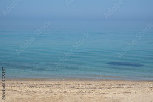 The calm surface of the sea and a deserted sandy beach. Small waves and blue sky. Halkidiki  Greece.