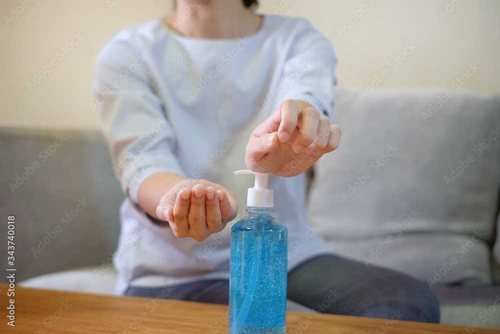 A woman squeezing a clear bottle of blue antibacterial gel on a wooden table to clean her hands.