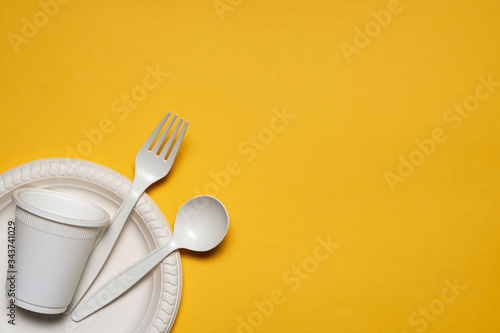 Photography disposable plate, glass, spoon and fork of corn starch on a yellow background
