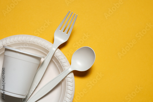 disposable plate, glass, spoon and fork of corn starch on a yellow background. biodegradable eco friendly picnic tableware. isolate. replacement of plastic with modern biomaterials. place for text