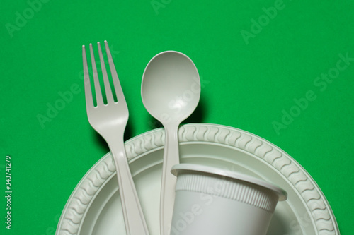 disposable spoon, fork, glass and plate of corn starch on a green background. biodegradable environmentally friendly dishes. isolate. replacement of plastic with modern biomaterials. 