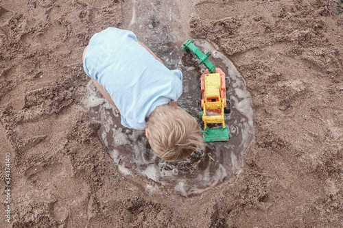 Little blonde boy playing with sand and water at the beach.