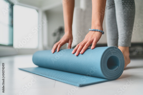 Yoga at home woman rolling exercise mat in living room of house or apartment condo for morning wellness yoga practice.
