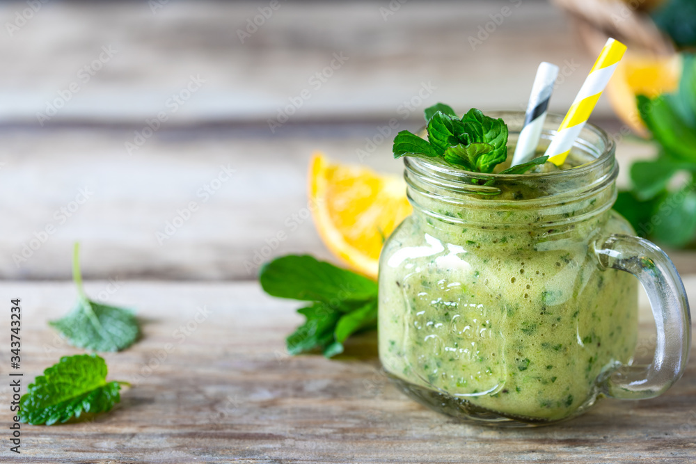 Homemade green smoothie in a jar with spinach, orange, apple and mint in glass jar and ingredients. Detox, diet, healthy, vegetarian food concept