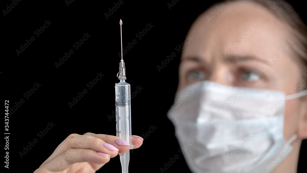 Close up of a syringe with a medicine vaccine in the hands of female doctor in white medical gown with sterile face mask on black background. Anti virus human health concept. Medicine and vaccination. Close up of a syringe with a medicine vaccine in the hands of female doctor in white medical gown with sterile face mask on black background. Anti virus human health concept. Medicine and vaccination.