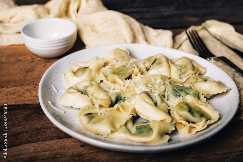 Italian ravioli with spinach, ricotta and parmesan cheese on top, close-up on a plate. rustic style on wooden table.