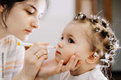 Makeup for baby. Mom and daughter play in a beauty salon at home where mom as a makeup artist applies makeup to her happy daughter