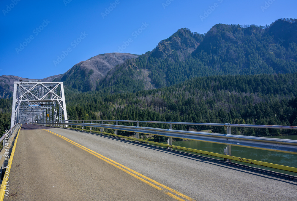Openwork web of transport metal bridge over the Columbia River amid majestic forested mountains