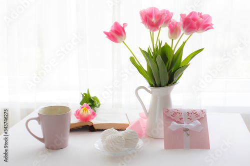 postcard good morning. Still life : a Cup of tea, a bouquet of pink tulips, marshmallows on a light background near the window.