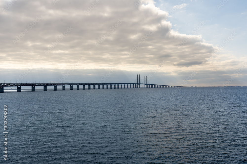 Oresundsbron between Copenhagen, Denmark and Malmo, Sweden with heavy clouds and sun rays shining through close to sunset. Wide angle view.