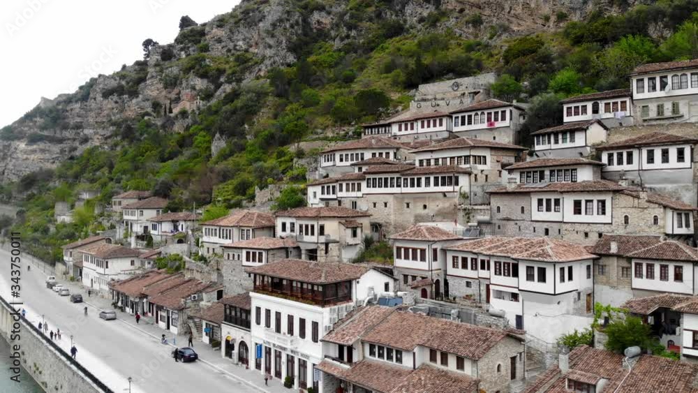 Traditional houses of Berat in Albania with white and stone walls, big windows and red roofs, built on riverside of rocky slope of mountain Traditional houses of Berat in Albania with white and stone walls, big windows and red roofs, built on riverside of rocky slope of mountain