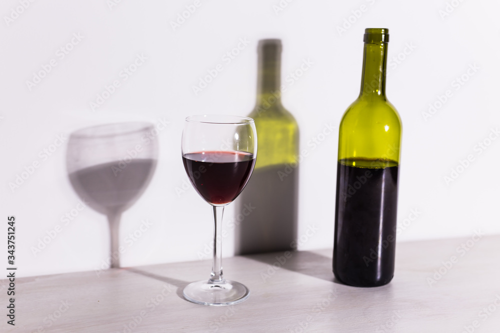A glass of wine and a bottle casts a long shadow from the evening sun. A glass of wine and a bottle casts a long shadow from the evening sun.
