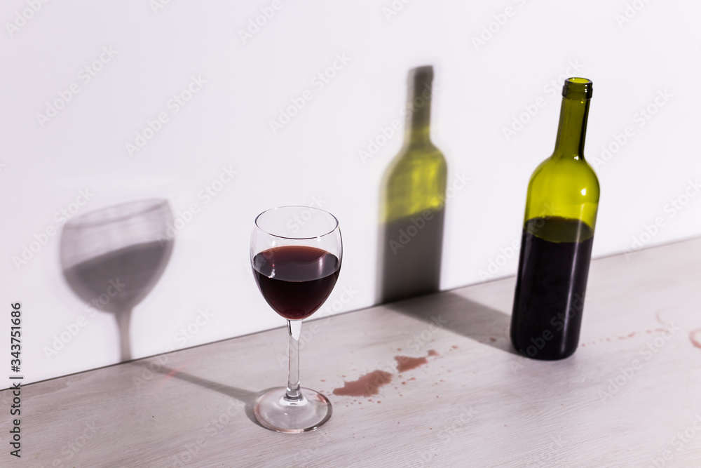Bottle with wine and glass, red puddle of wine on the table. Cleaning after party concept.