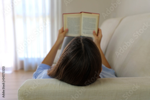 Close up of lying woman reading book relaxing at home. Back view of girl lying on couch enjoying reading a book.