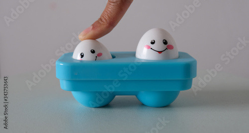 Valokuva jouet de bébé avec deux œufs dans un socle bleu - Un doigt écrase un des œuf