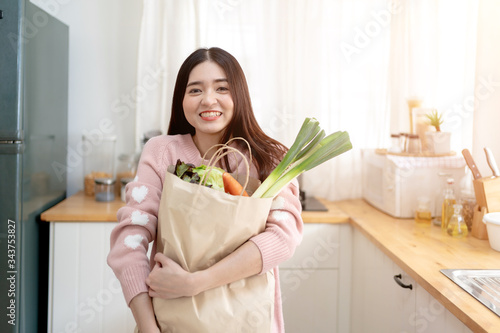 Asian Young Woman Holding Grocery Shopping Bag with vVegetables Standing in the kitchen