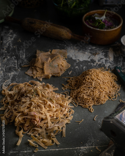 Process of making homemade wholewheat pasta in a kitchen with pasta sheet roller. Close up view. Dark photography