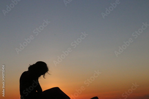 silhouette of a woman "Kupang, Indonesia - 28 April 2020: a woman sitting on the beach enjoying the sunset. East Nusa Tenggara Province, Indonesia on 7 October 2017". © Dedi