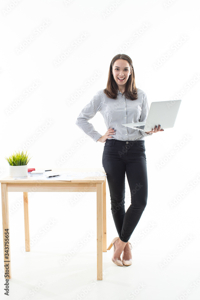 The brunette is standing next to the table and working on a computer on a white background