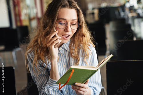 Image of cheerful young woman talking on cellphone and holding planner