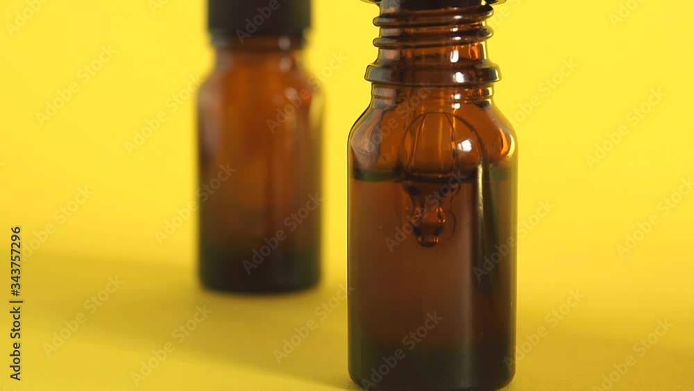 Drop falls from the pipette. Bottle of cosmetic oil serum on the table. Yellow background with copy space. Drop falls from the pipette. Bottle of cosmetic oil serum on the table. Yellow background with copy space.