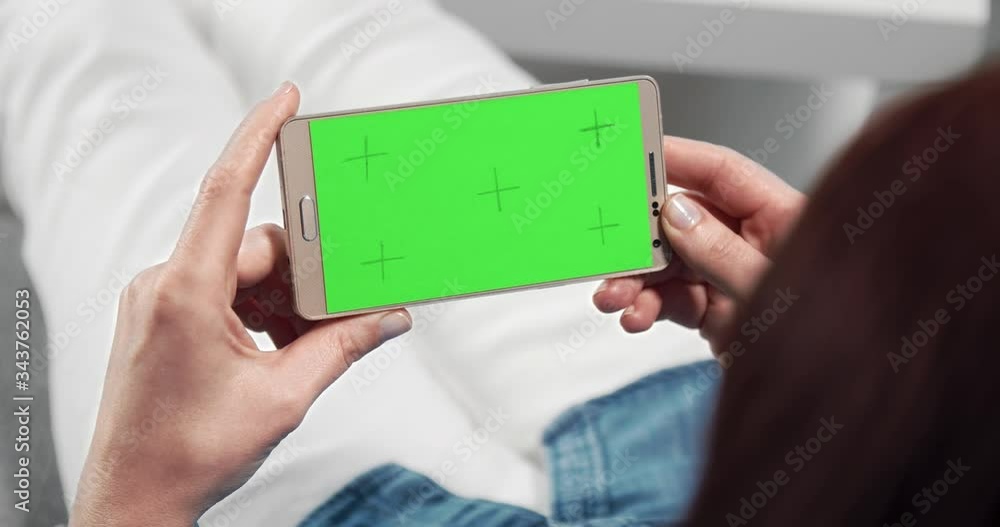 Close up of smartphone with blank green screen that holding woman in hands while relaxing on comfortable couch. Concept of modern device and leisure time Close up of smartphone with blank green screen that holding woman in hands while relaxing on comfortable couch. Concept of modern device and leisure time