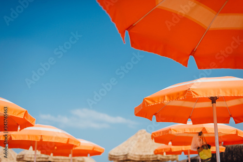 Fototapeta Naklejka Na Ścianę i Meble -  Summer blue sky, view through orange umbrellas. Summer vacation at the beach
