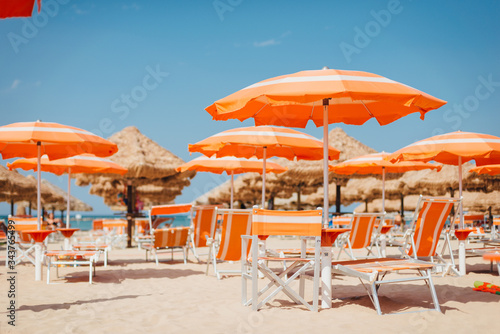 Fototapeta Naklejka Na Ścianę i Meble -  Beach in Italy. Orange umbrellas and deck chairs on the sand against the sea. Summer time