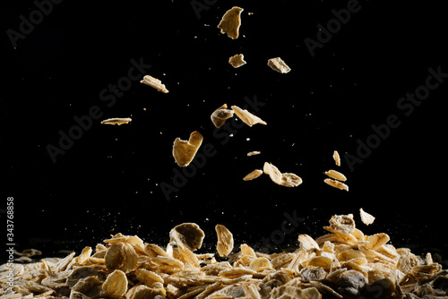 Whole oats being poured onto counter, oatmeal on a black background