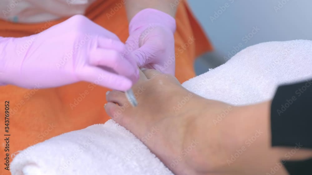 Pedicurist master in gloves polishing client's toe nails using file, hands closeup. Professional pedicure in beauty salon. Hygiene and care for feet. Beauty industry concept. Pedicurist master in gloves polishing client's toe nails using file, hands closeup. Professional pedicure in beauty salon. Hygiene and care for feet. Beauty industry concept.