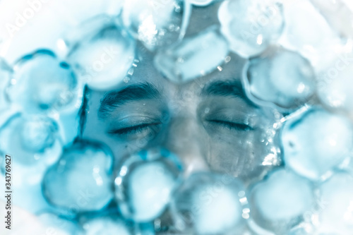 Male face with eyes closed on ice cubes, simulation of freezing