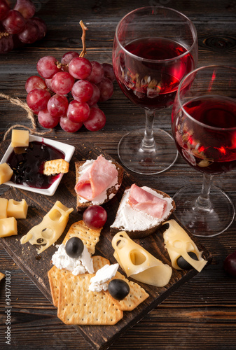 glasses of wine , appetizer, tapas, slices of cheese, cracker, ham, jam, grapes, olives, on a dark wooden background, top view