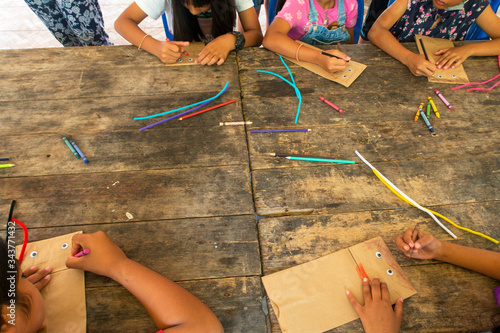Top view of Asian kid & children group learning how to make paper puppet toy on wooden table background during free time or weaken, preschool or kindergarten daycare education concept, copy space 