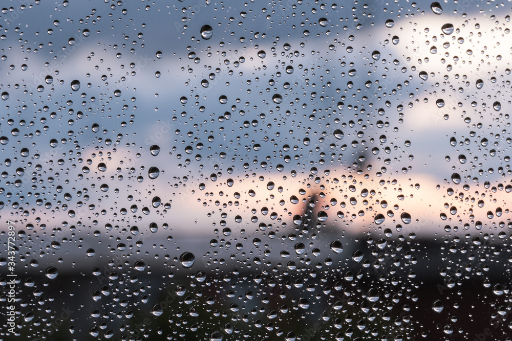 Horizontal frame of rain drops on window glass at sunset in the city