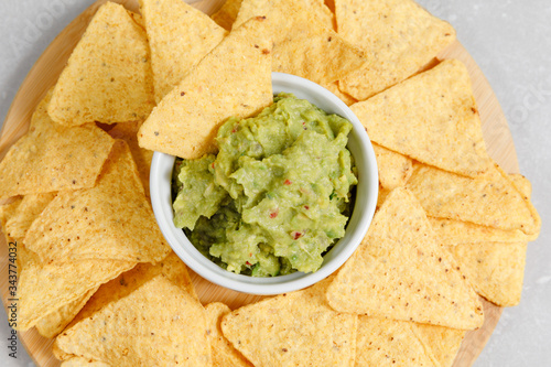 Guacamole sauce with nachos on a round wooden plate