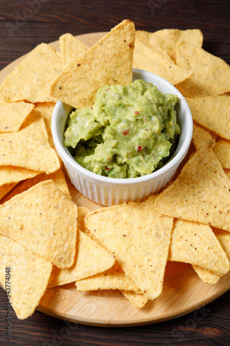 Guacamole sauce served with nachos on a wooden background