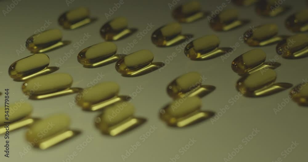Vitamin supplement cod liver oil capsules in a line reflect liquid inside as light moves across. Vitamin supplement cod liver oil capsules in a line reflect liquid inside as light moves across.