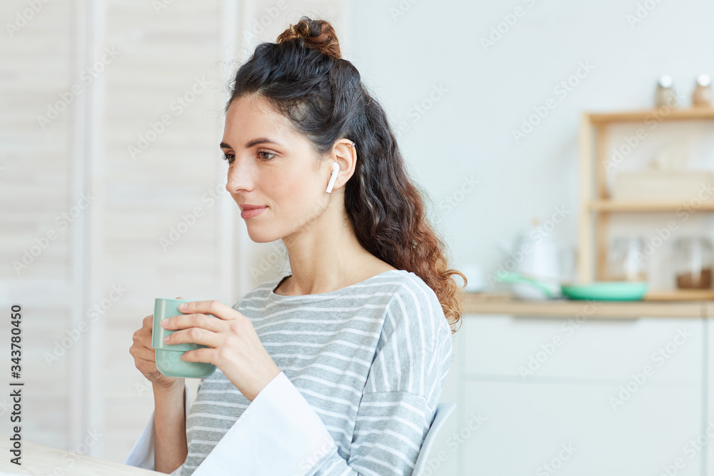 Portrait of young adult Caucasian woman spending morning at home drinking tea and listening to music in her wireless earphones Portrait of young adult Caucasian woman spending morning at home drinking tea and listening to music in her wireless earphones