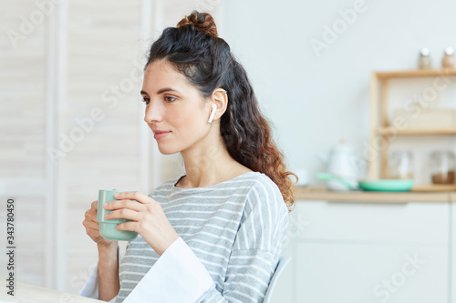 Portrait of young adult Caucasian woman spending morning at home drinking tea and listening to music in her wireless earphones