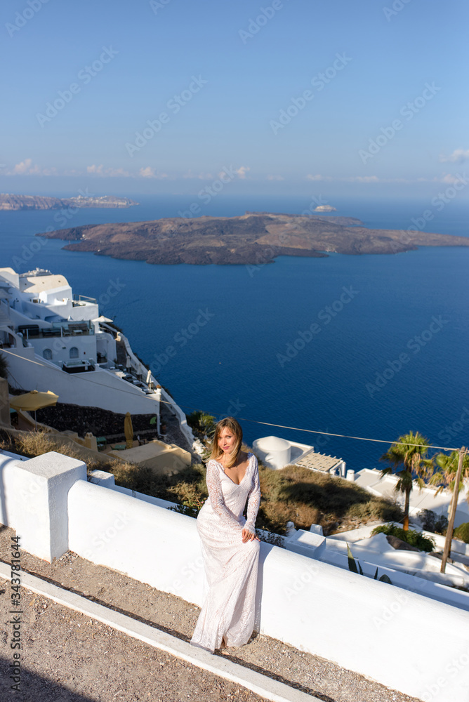 Beautiful bride In a white dress posing against the background of the Mediterranean Sea in Thira, Santorini.