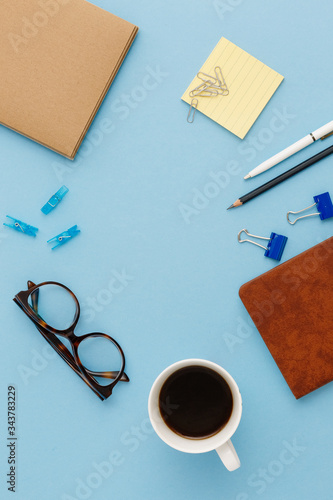 Blank brown vintage notebook, leaves, pencil, pen, diary, cup of coffee, paper clips, glasses on colorful blue table. Stylish minimalistic workplace concept. Top view with copy space.