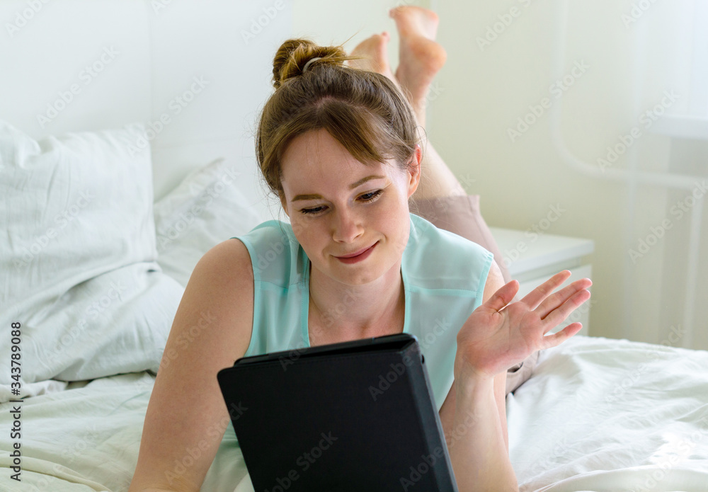 Happy young woman laying in bed and making videocall using tablet Happy young woman laying in bed and making videocall using tablet