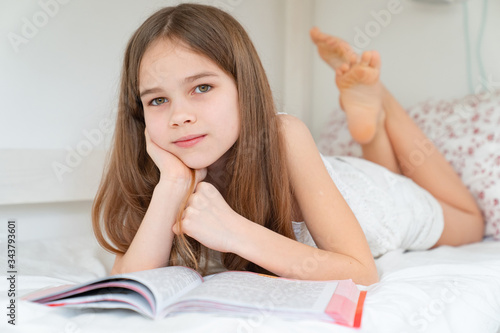 school concept. little girl with book lying on bed